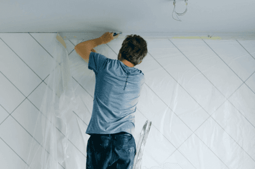 Man on a ladder fixing something on the wall